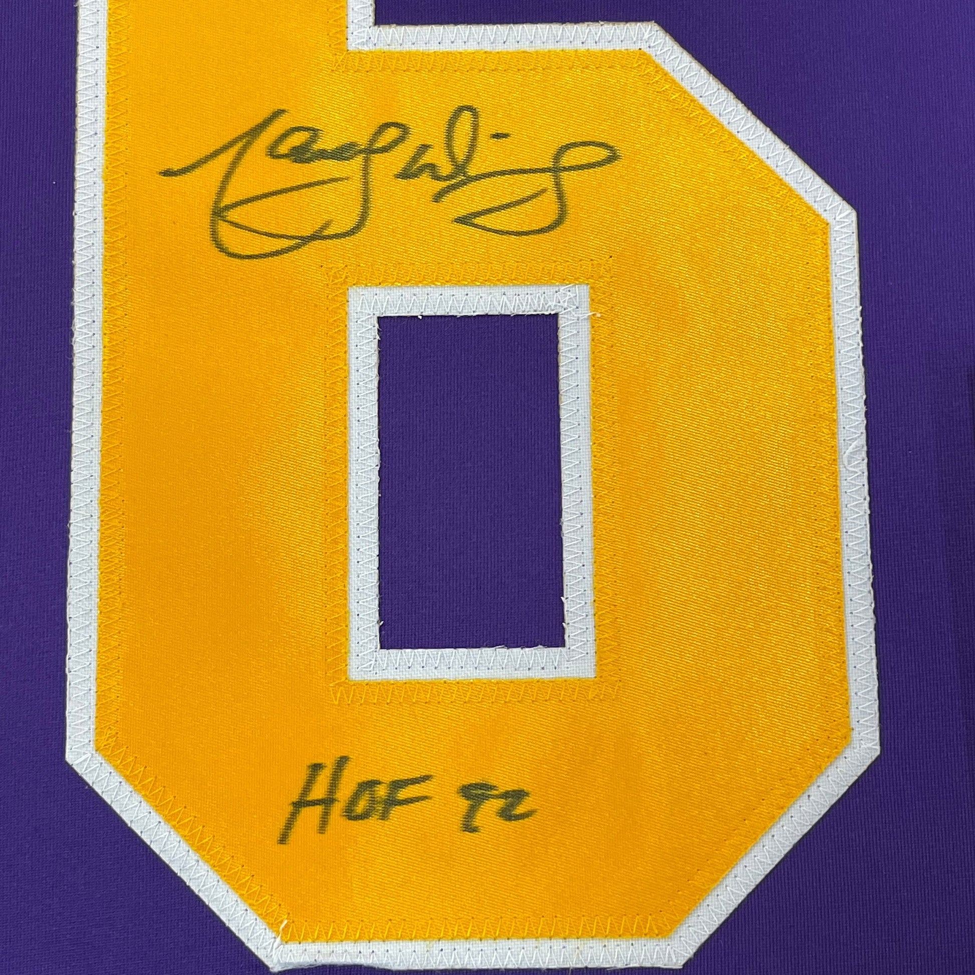 Close-up of yellow jersey patch with white border showing signed autograph and "HOF 76" text on purple fabric background.