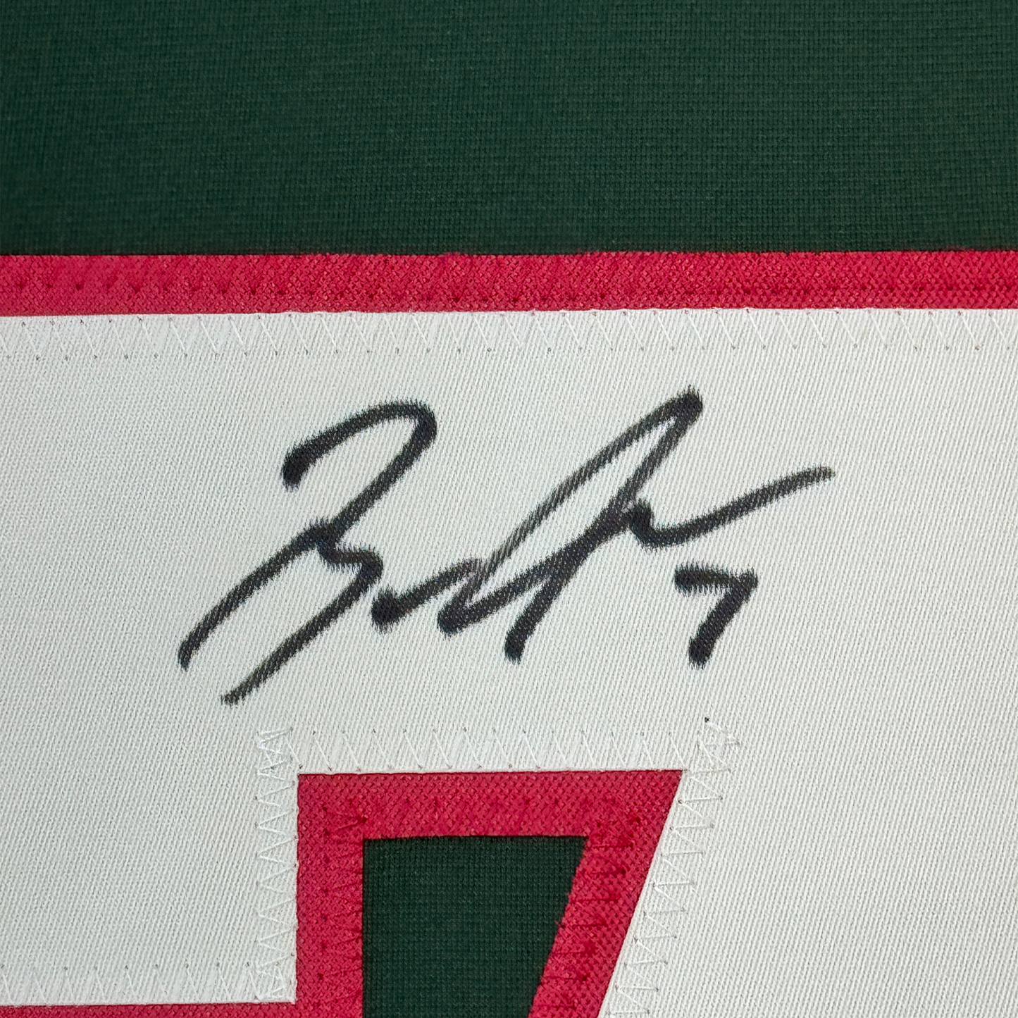 Close-up of handwritten signature on white fabric strip of Minnesota hockey jersey with red and green stripes.