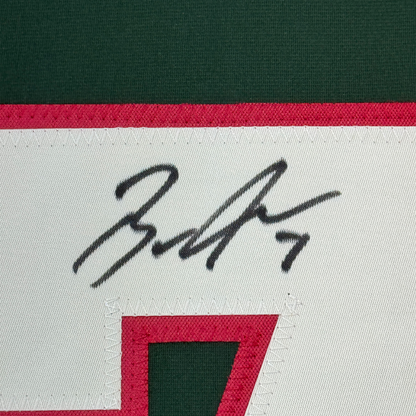 Close-up of handwritten signature on white fabric strip of Minnesota hockey jersey with red and green stripes.