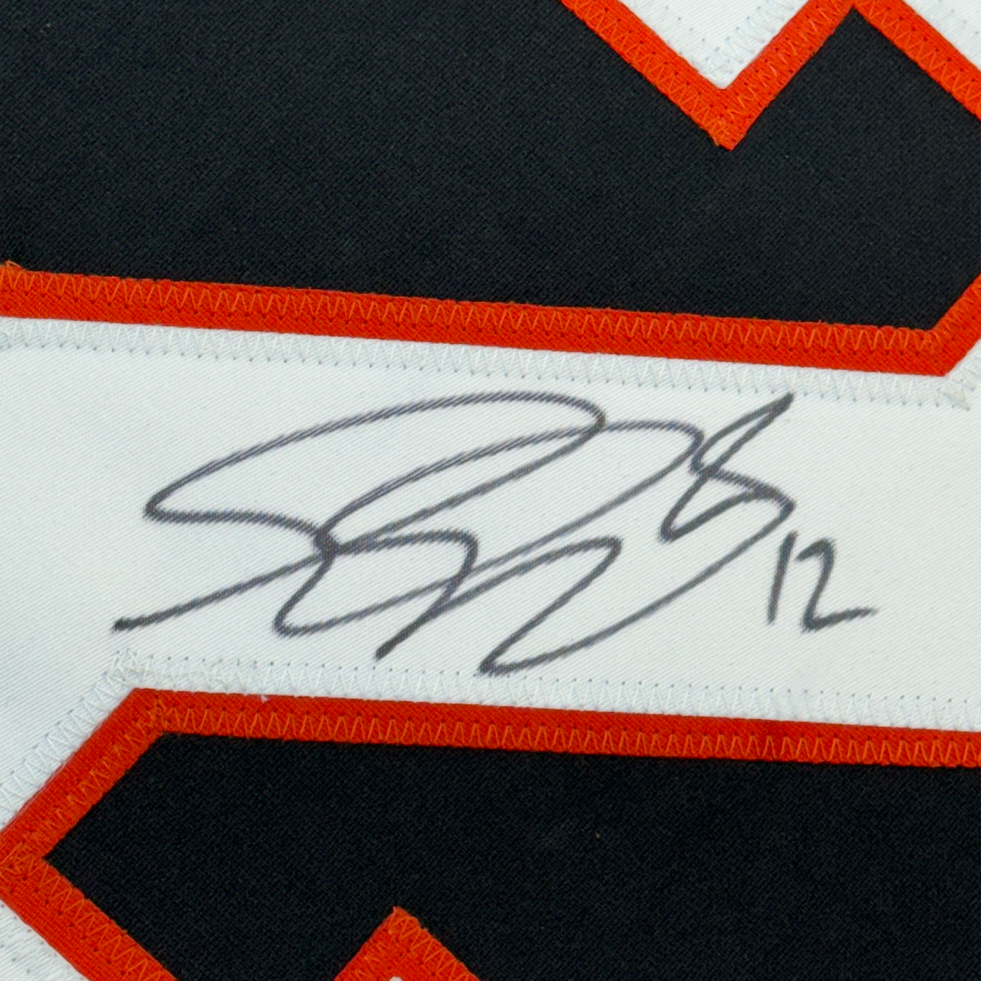 Close-up of handwritten signature in blue ink on white fabric stripe with red and black hockey jersey trim visible.