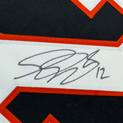Close-up of handwritten signature in blue ink on white fabric stripe with red and black hockey jersey trim visible.