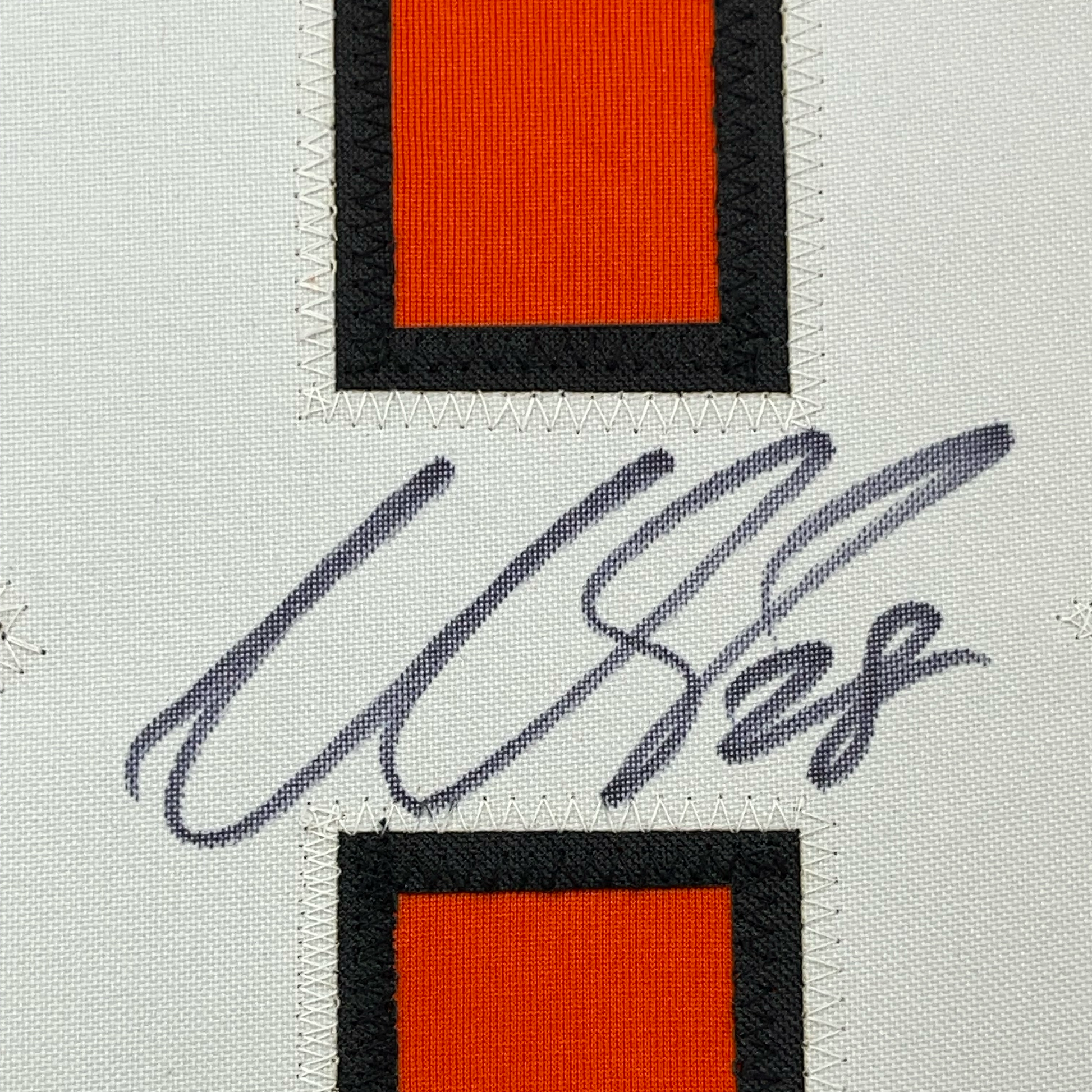 Close-up of autograph signature in dark ink on cream fabric between two framed orange and black jersey sections with zigzag stitching.