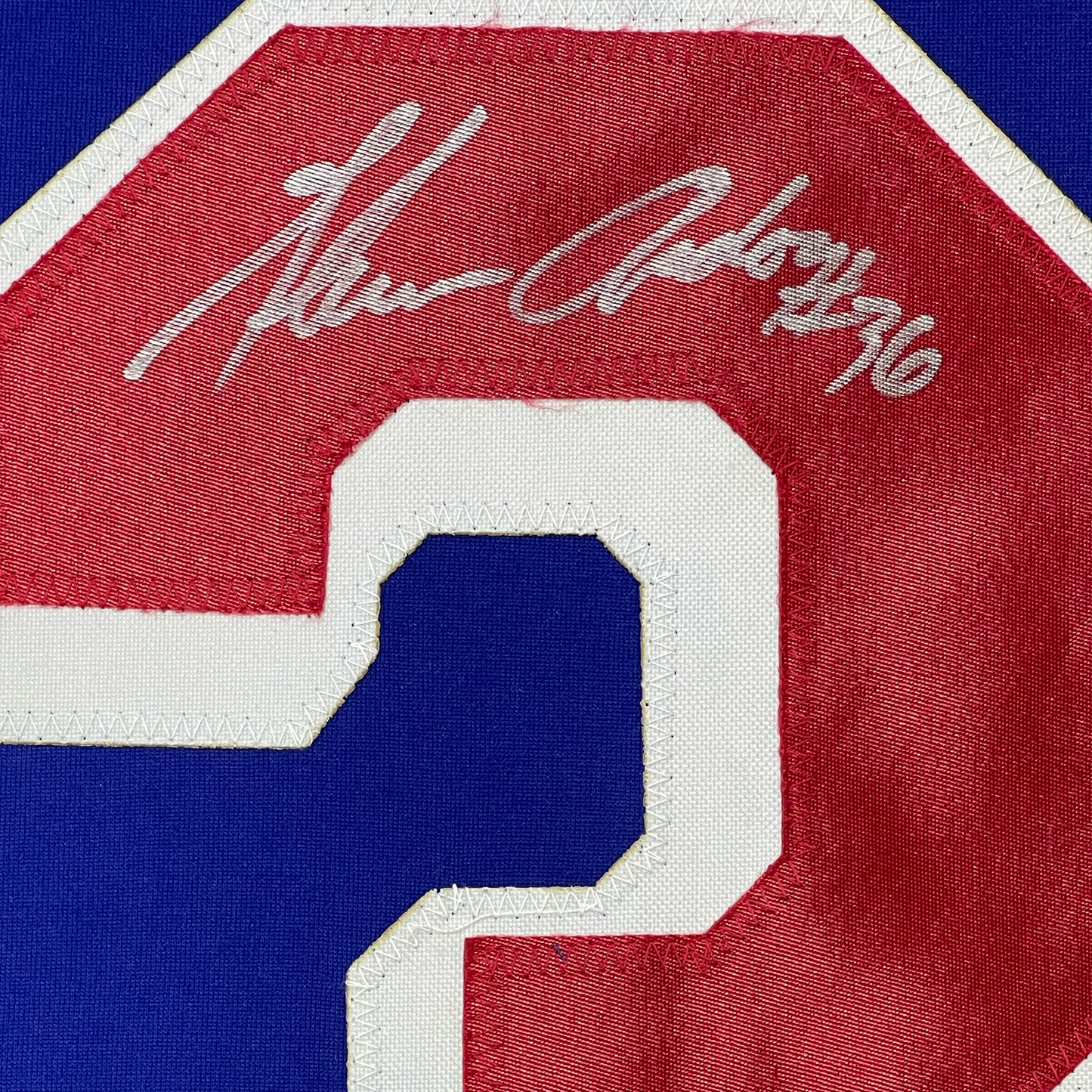 Close-up detail of embroidered number 9 on red, white, and blue hockey jersey with partial signature visible above.