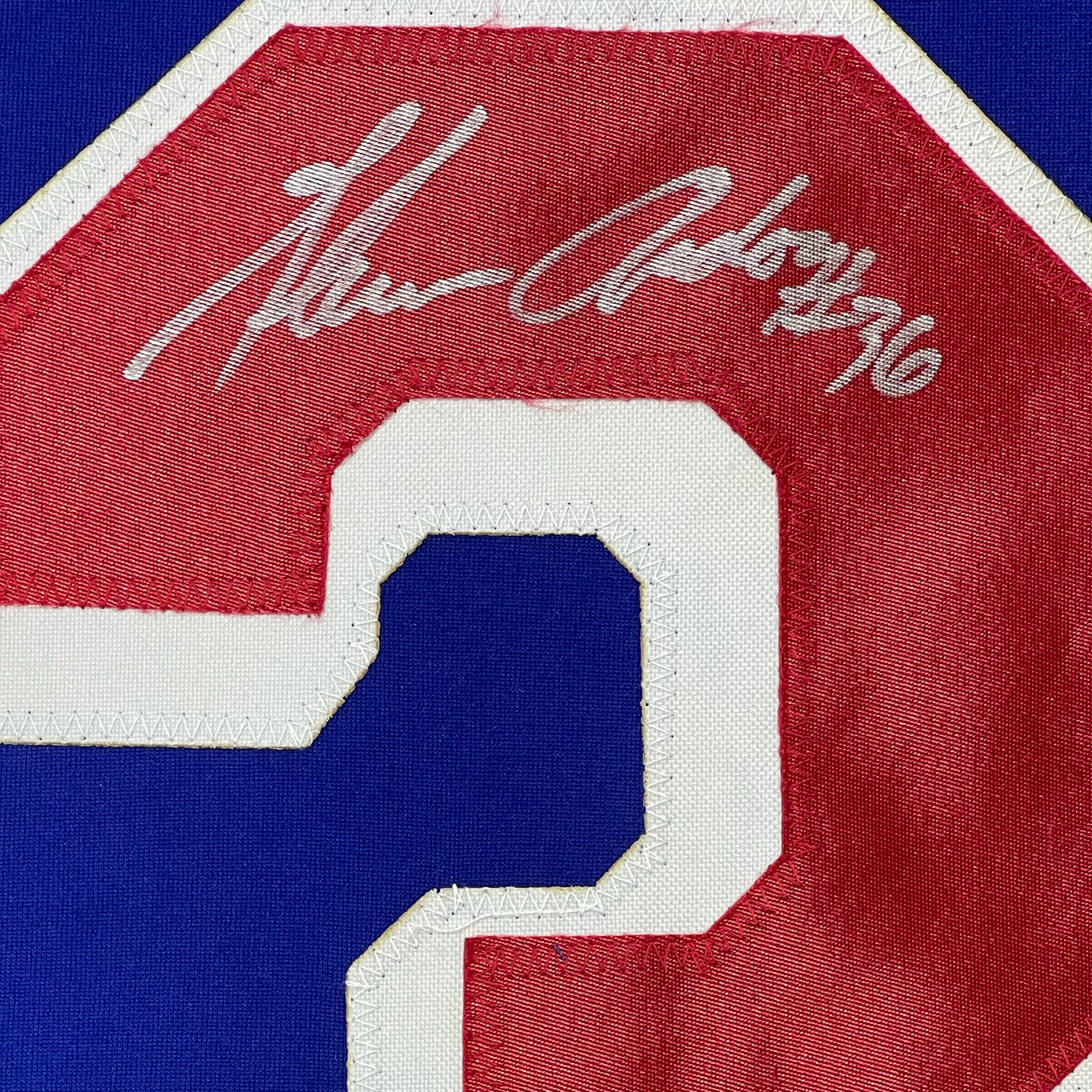 Close-up detail of embroidered number 9 on red, white, and blue hockey jersey with partial signature visible above.
