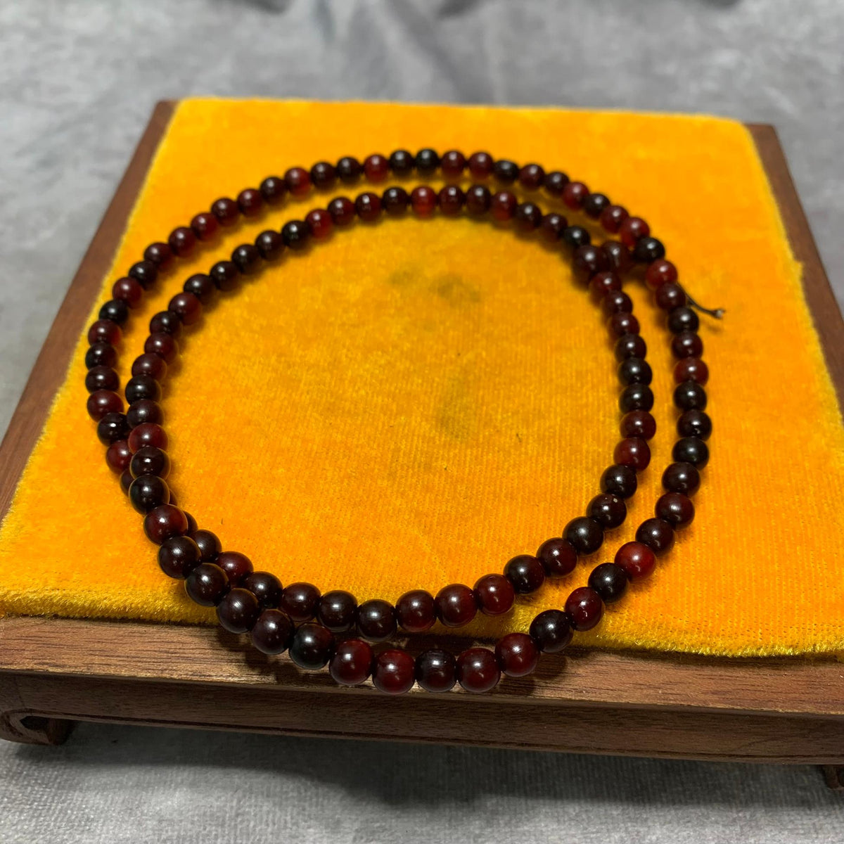 The cherry red horn bead strand coiled in two loops on a yellow cushion stand