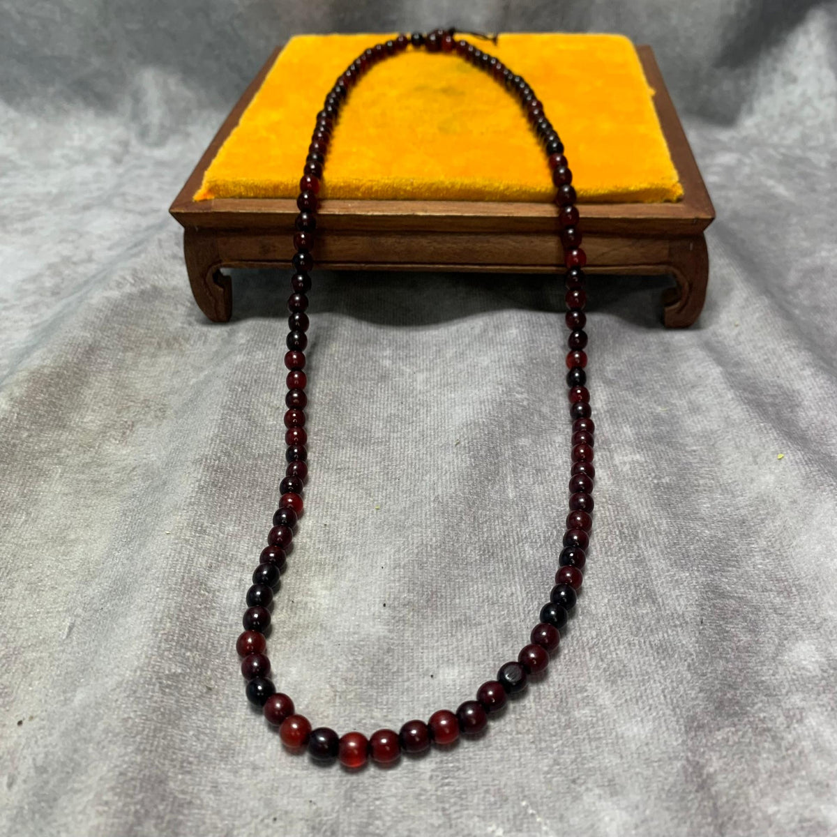 The 26-inch horn bead necklace draped over a small wooden stand, hanging as a single strand