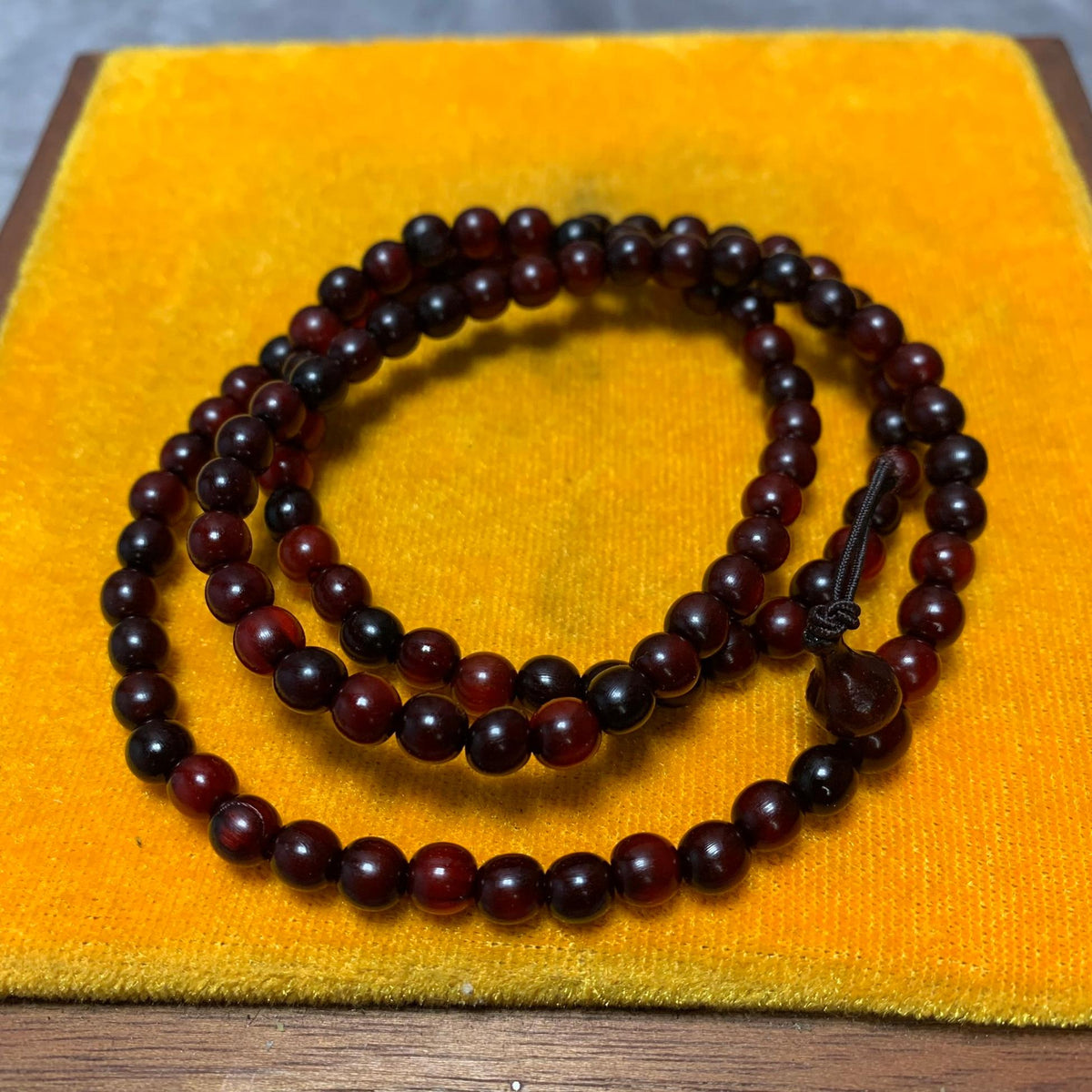 Close-up of the horn beads coiled on a yellow cushion, showing the bead grain and the gourd-shaped head bead tied off with a decorative knot