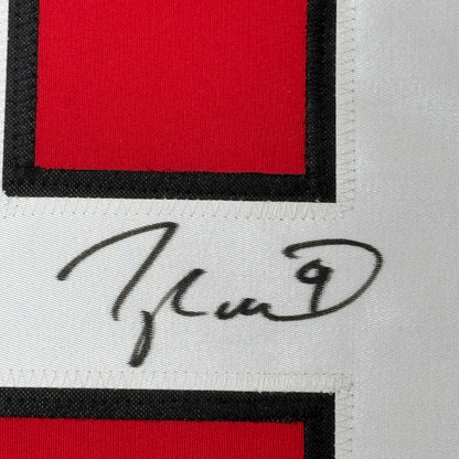 Close-up of handwritten signature on white fabric strip between red and black sections of jersey.