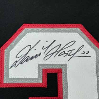 Close-up of handwritten signature on white jersey nameplate with red and gray stitched borders.