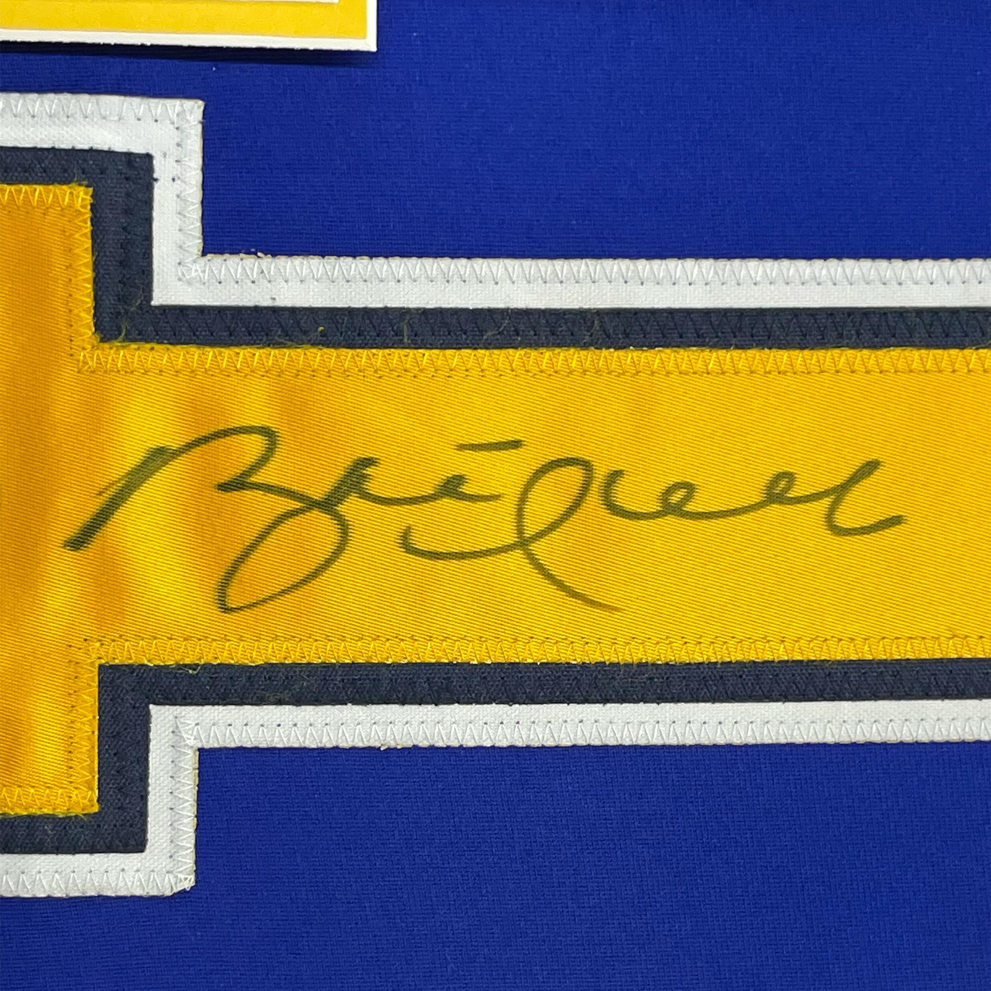 Close-up of handwritten signature in dark ink on yellow stripe of blue and yellow hockey jersey with white and black trim.