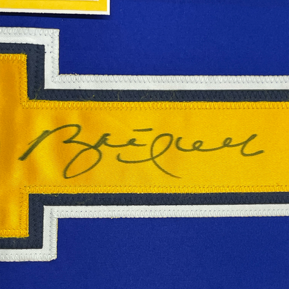 Close-up of handwritten signature in dark ink on yellow stripe of blue and yellow hockey jersey with white and black trim.