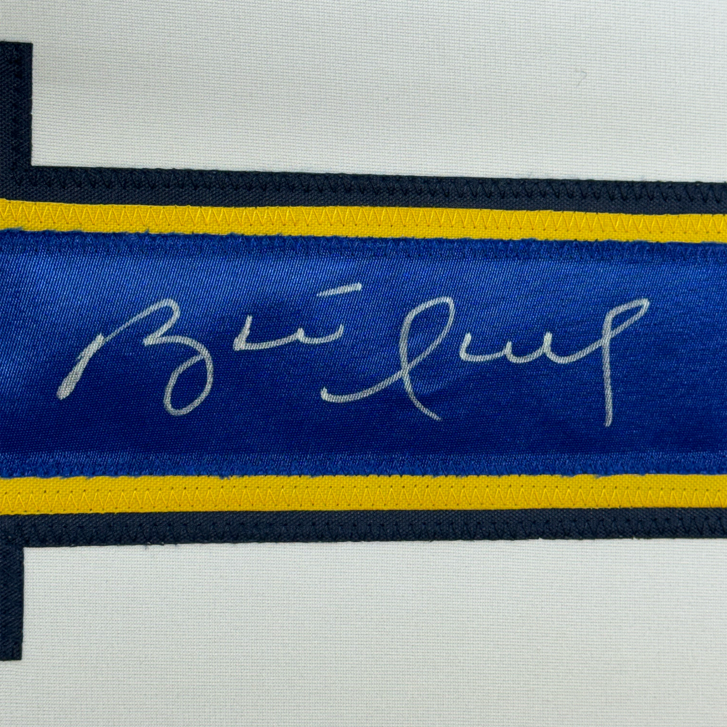Close-up of blue hockey jersey stripe with handwritten signature in silver ink, yellow and black trim visible.