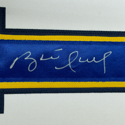 Close-up of blue hockey jersey stripe with handwritten signature in silver ink, yellow and black trim visible.