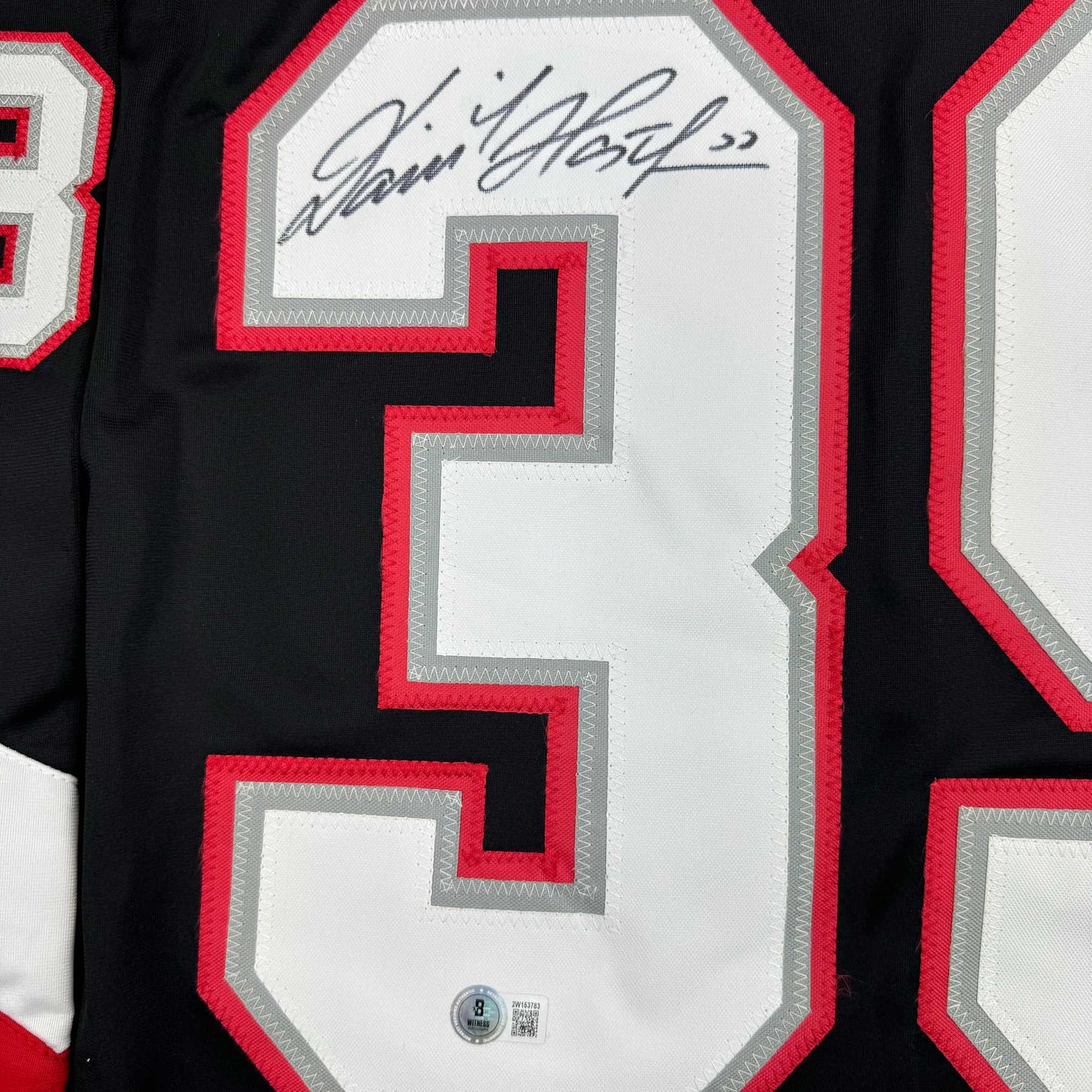 Close-up of signed number 39 on black hockey jersey with red and gray trim and Beckett authentication hologram.