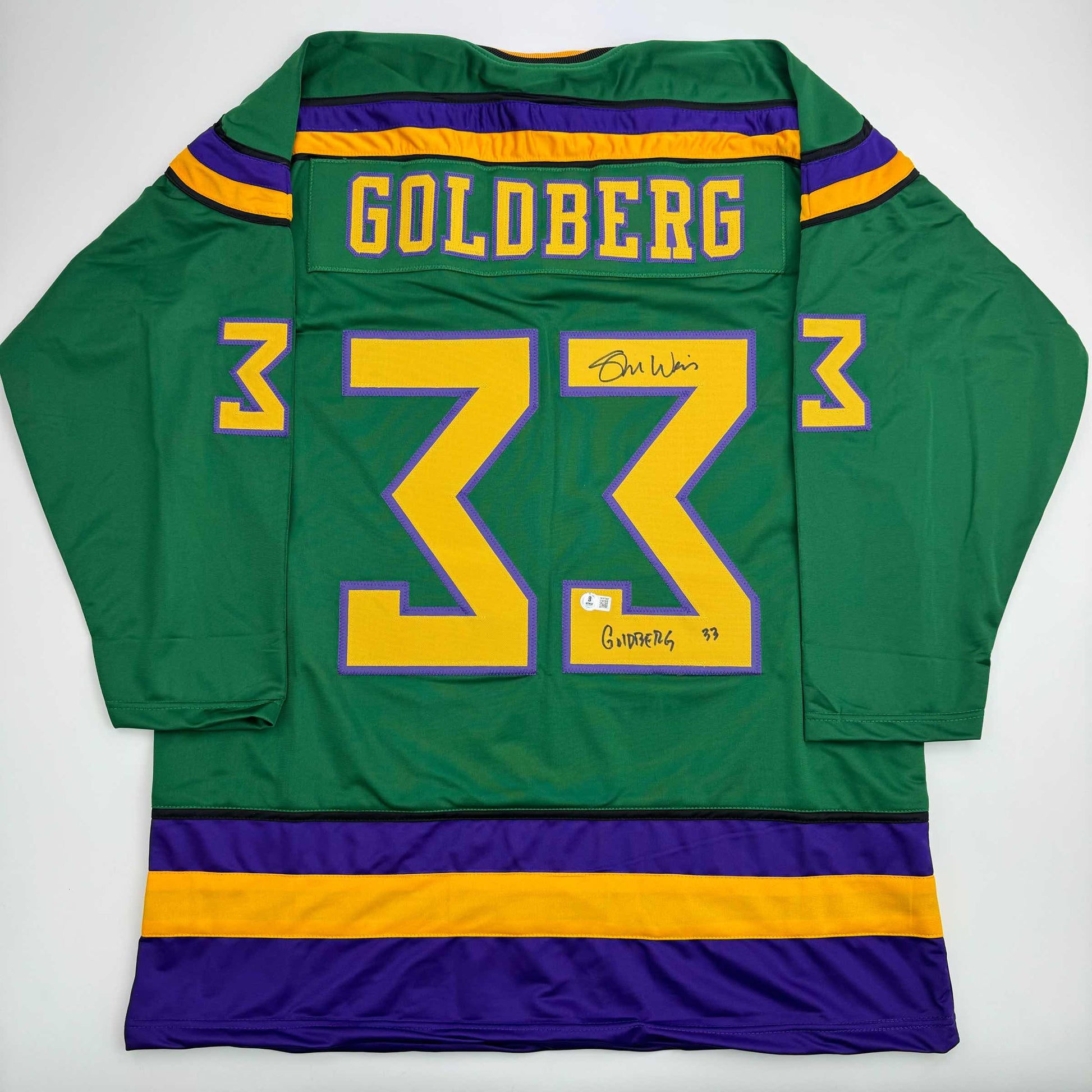 Back view of green hockey jersey with yellow number 33, purple and gold stripes, Goldberg nameplate, and autographed signatures.