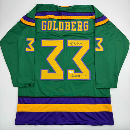 Back view of green hockey jersey with yellow number 33, purple and gold stripes, Goldberg nameplate, and autographed signatures.