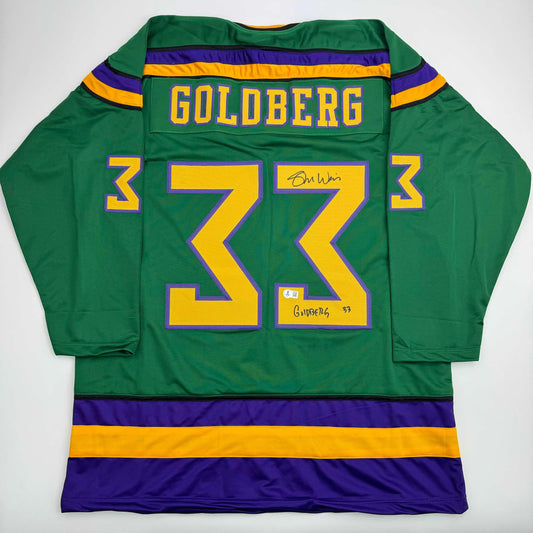 Back view of green hockey jersey with yellow number 33, purple and gold stripes, Goldberg nameplate, and autographed signatures.