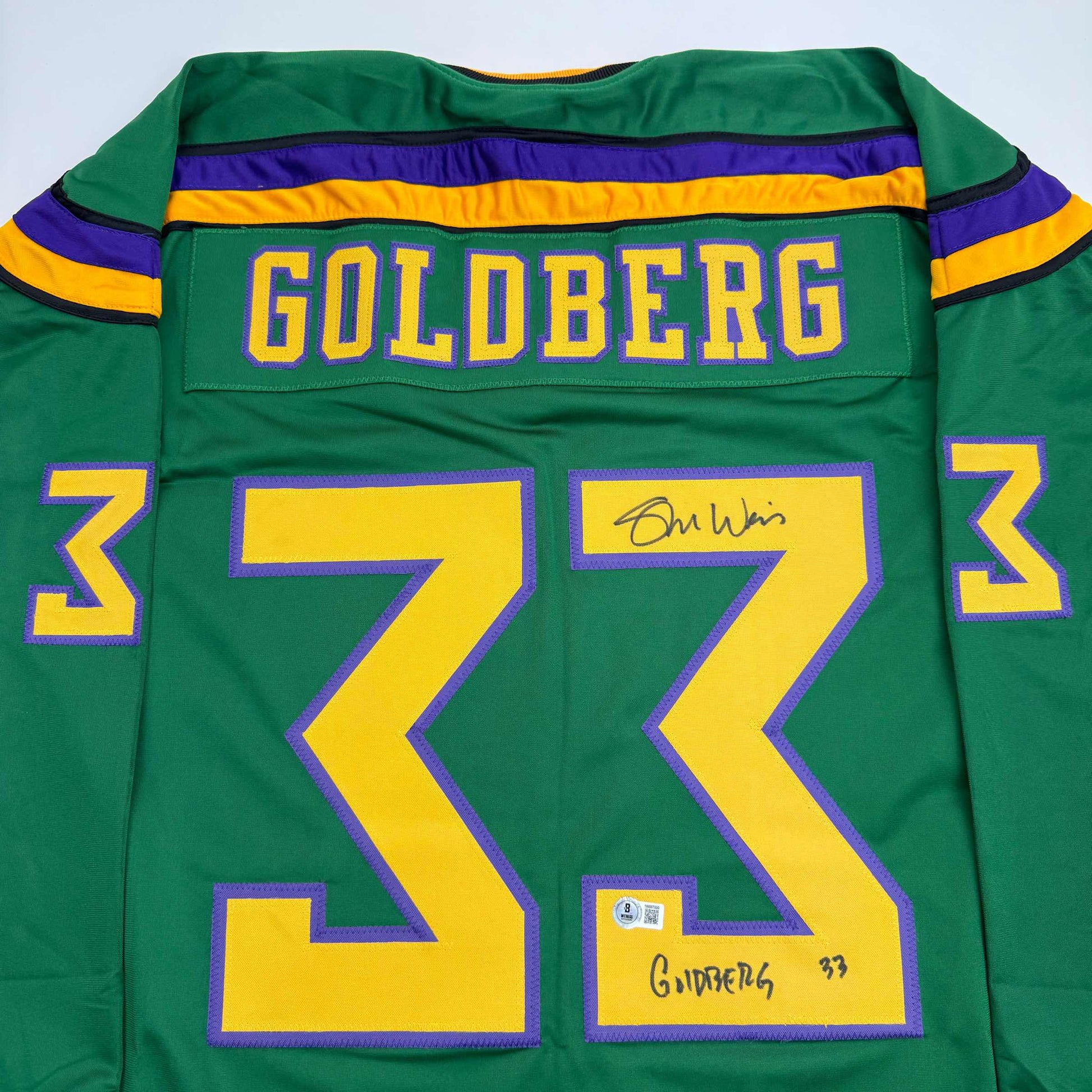 Back view of green Mighty Ducks hockey jersey number 33 with "GOLDBERG" nameplate and purple/yellow trim, signed by player.
