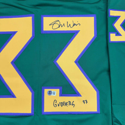 Close-up of signed green hockey jersey showing yellow number 99 with purple trim and "Goldberg" handwritten below with Beckett authentication sticker.