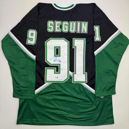 Flat lay of signed black and green Dallas hockey jersey displaying Seguin number 91 with visible autograph on white chest numbers.