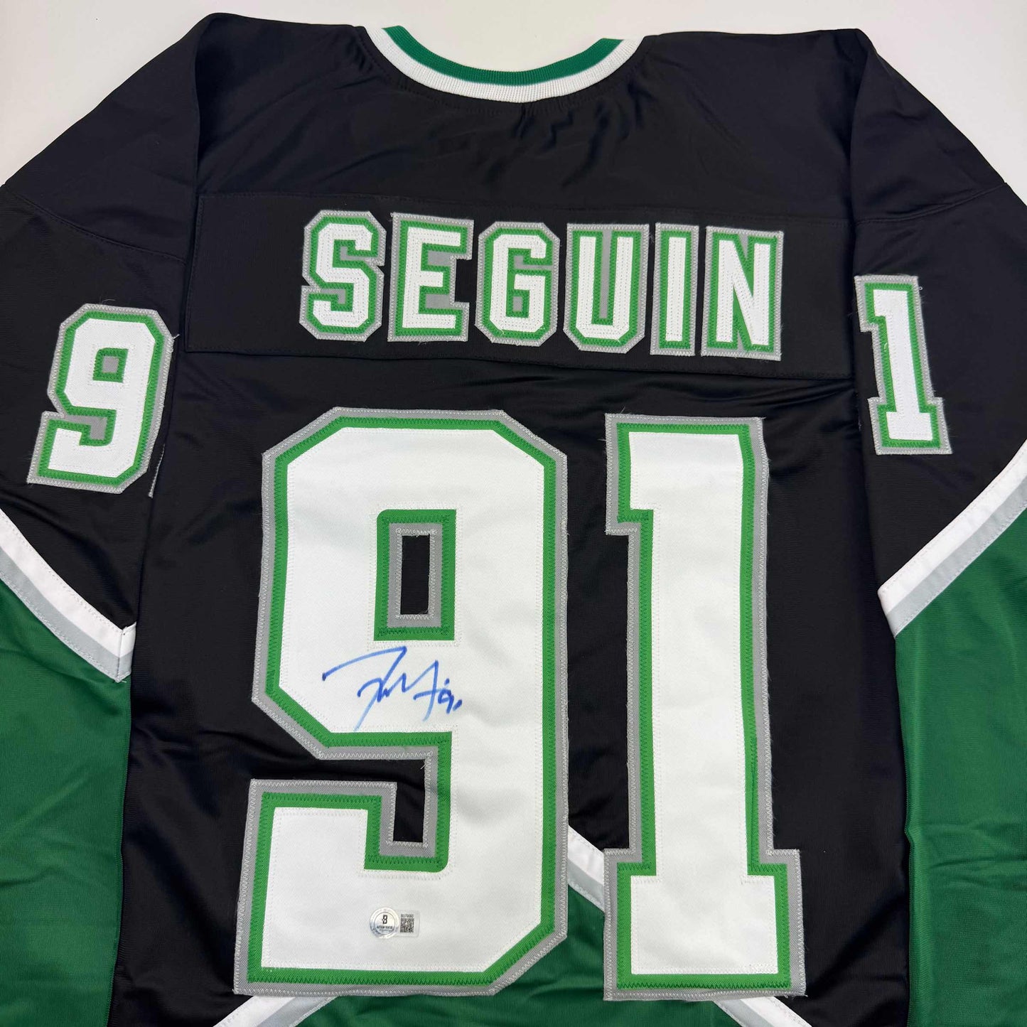 Back view of black hockey jersey with green and white "SEGUIN" and number 91, featuring blue autograph on white chest panel.