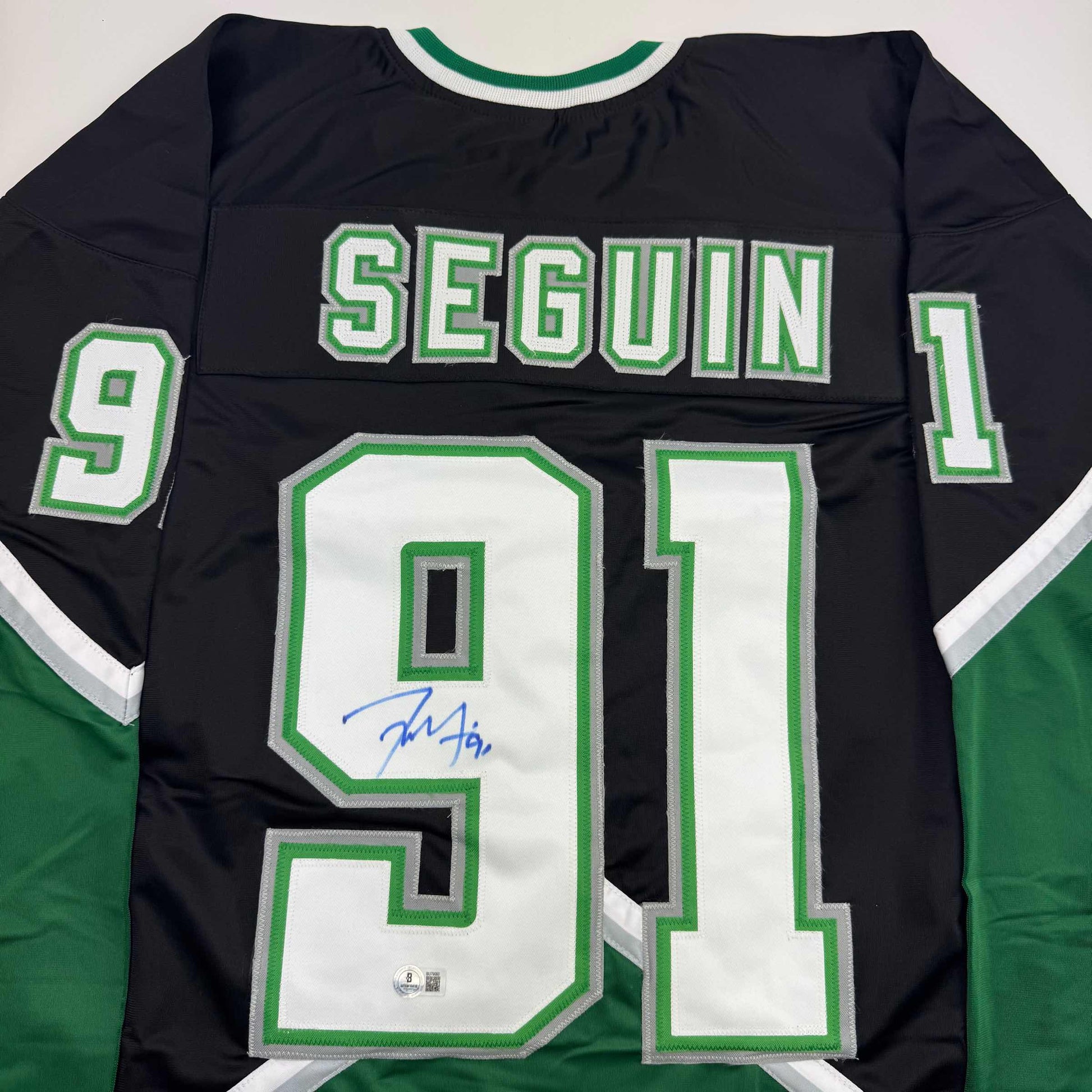 Back view of black hockey jersey with green and white "SEGUIN" and number 91, featuring blue autograph on white chest panel.