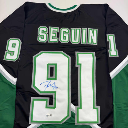 Back view of black hockey jersey with green and white "SEGUIN" and number 91, featuring blue autograph on white chest panel.