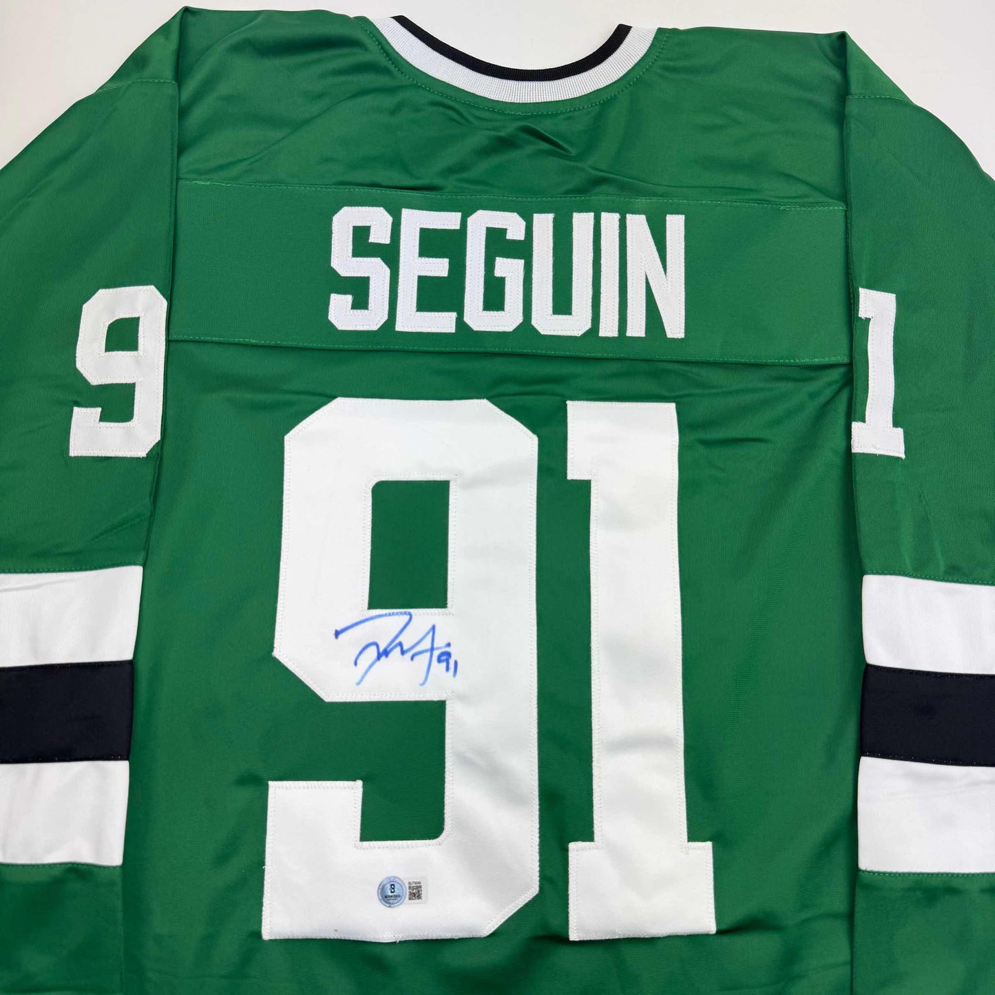 Back view of green hockey jersey with white "SEGUIN" nameplate and number 91, signed in blue ink, white and black striping on sleeves.