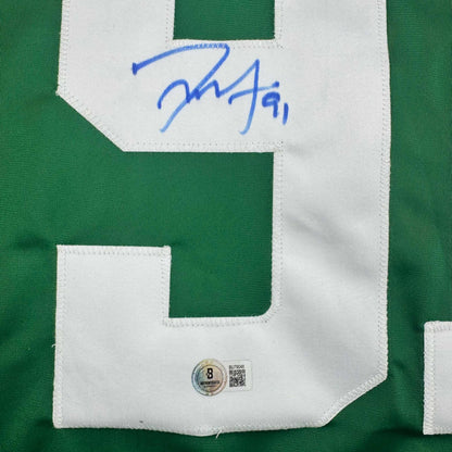 Close-up of signed green and white hockey jersey showing blue autograph and Beckett authentication hologram on white nameplate area.