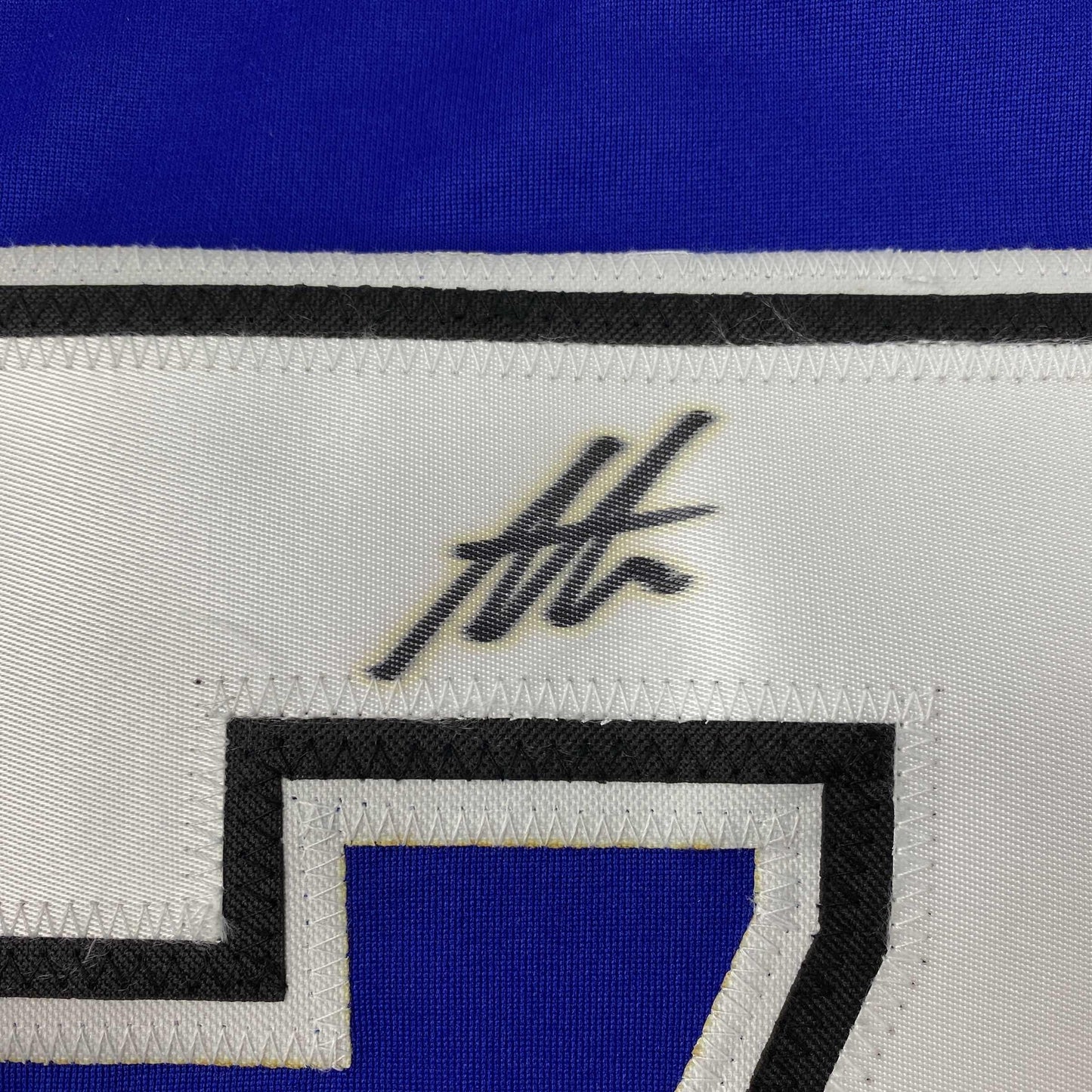 Close-up of white jersey fabric showing black handwritten signature and striped trim in blue, black, and white.