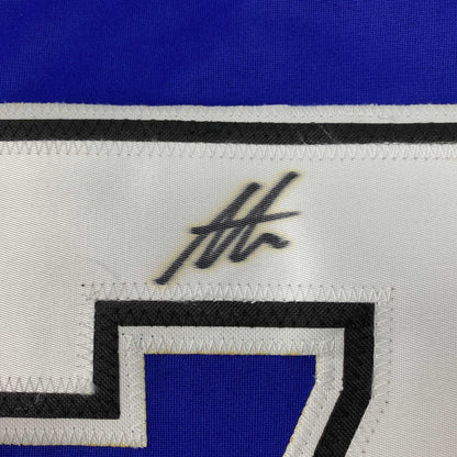 Close-up of white jersey fabric showing black handwritten signature and striped trim in blue, black, and white.