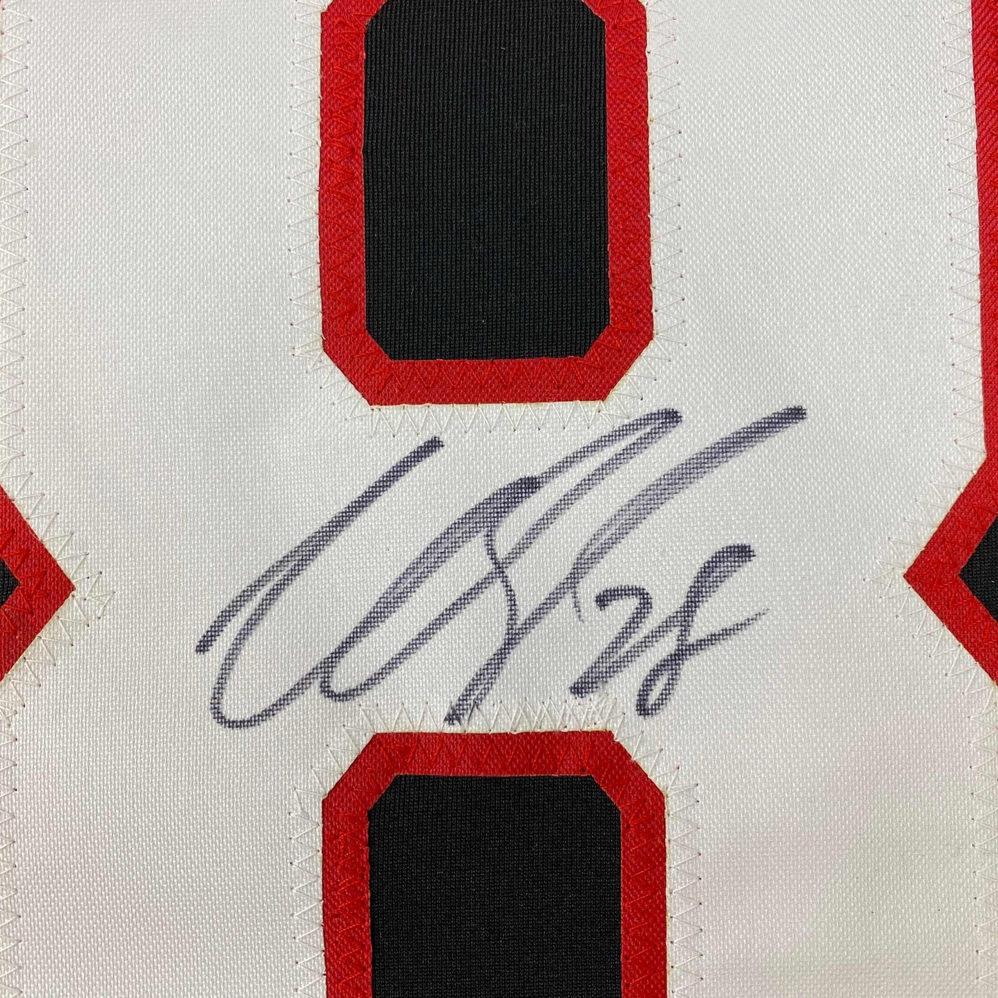Close-up of handwritten signature in blue ink on white jersey card with red and black diamond design elements.