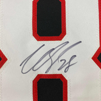 Close-up of handwritten signature in blue ink on white jersey card with red and black diamond design elements.