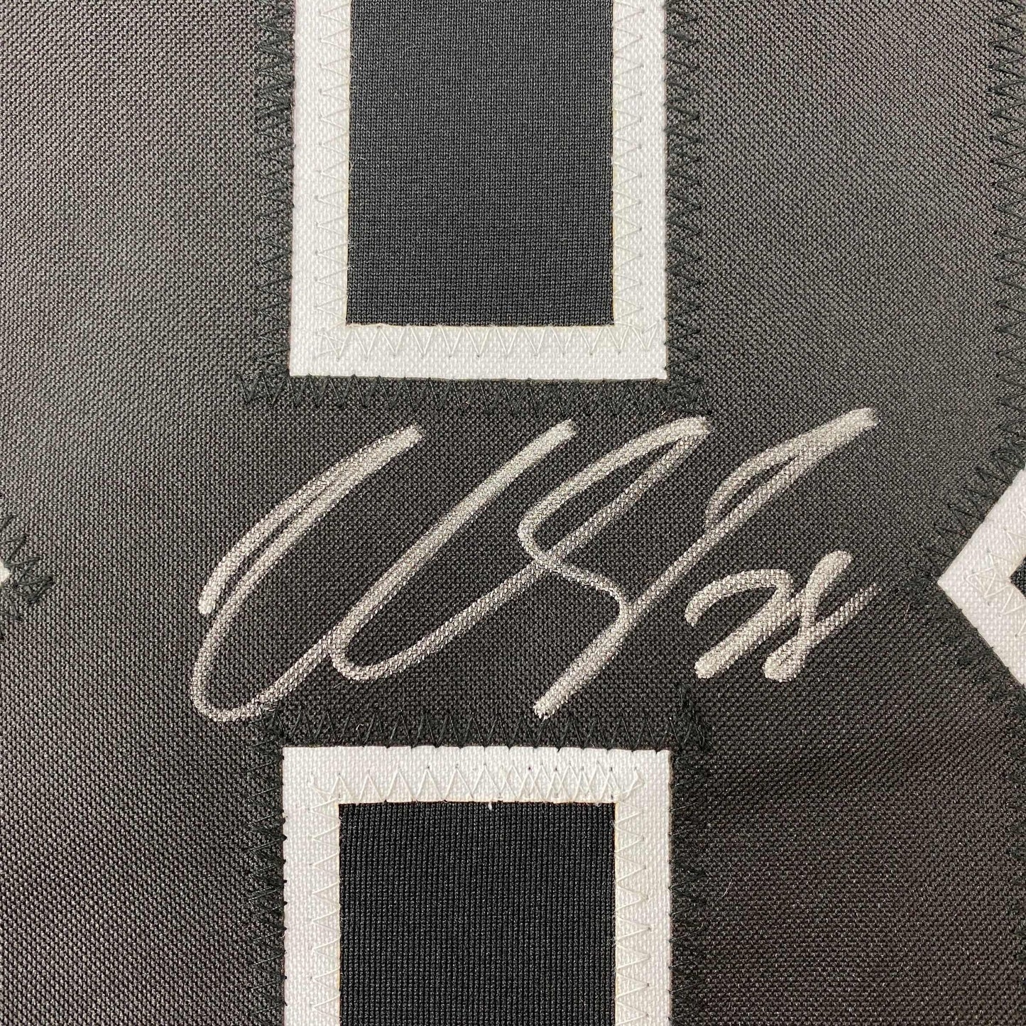 Close-up of autographed Claude Giroux signature in white ink on black hockey jersey fabric with white trim.