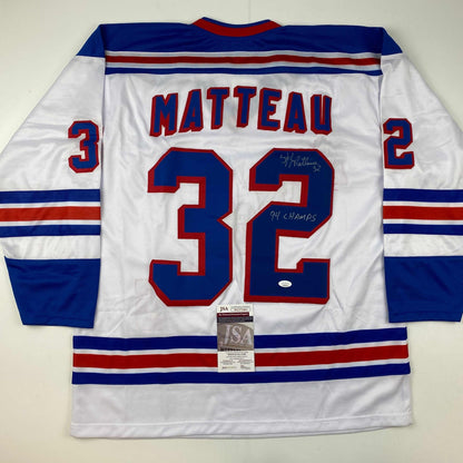 Back view of white hockey jersey with blue and red stripes, displaying "MATTEAU 32" in red numbers with handwritten signature and "94 CHAMPS" inscription, JSA authentication certificate visible at bottom.