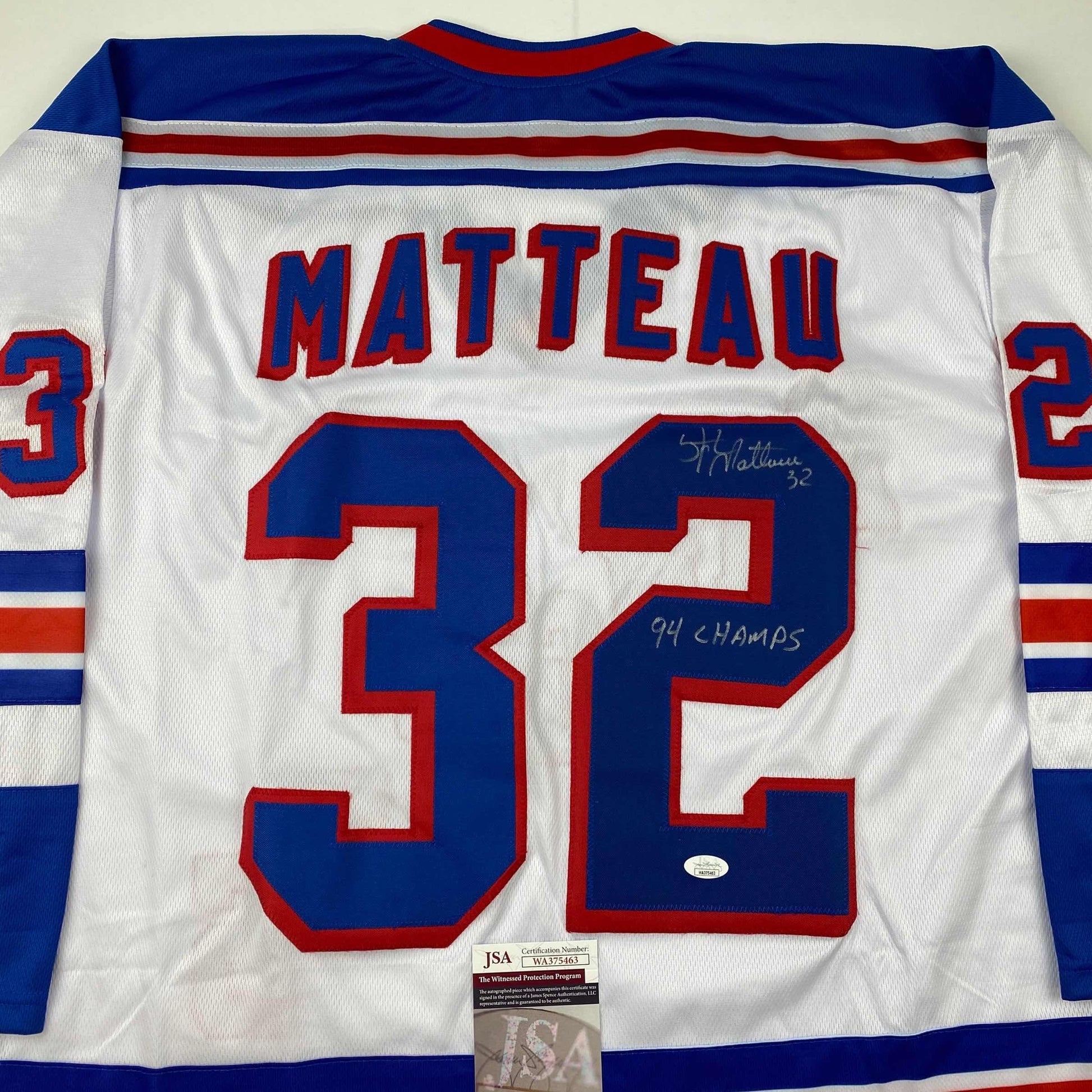 Back view of white hockey jersey with blue and red stripes, displaying "MATTEAU" and number "32" with handwritten autograph and "94 CHAMPS" inscription, JSA authentication label visible at bottom.