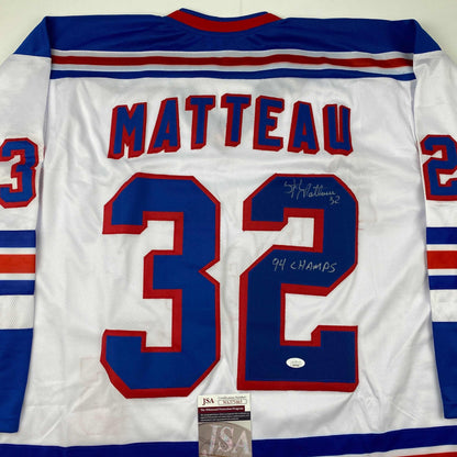 Back view of white hockey jersey with blue and red stripes, displaying "MATTEAU" and number "32" with handwritten autograph and "94 CHAMPS" inscription, JSA authentication label visible at bottom.