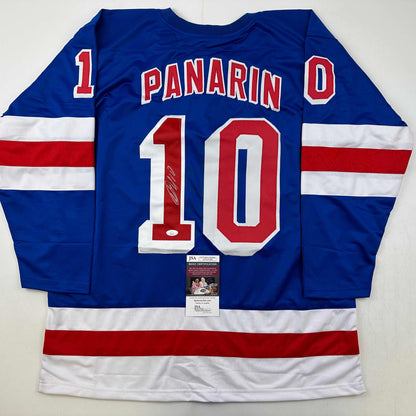 Blue hockey jersey with red and white stripes displaying "PANARIN" and number "10" with autograph and JSA certification sticker visible.