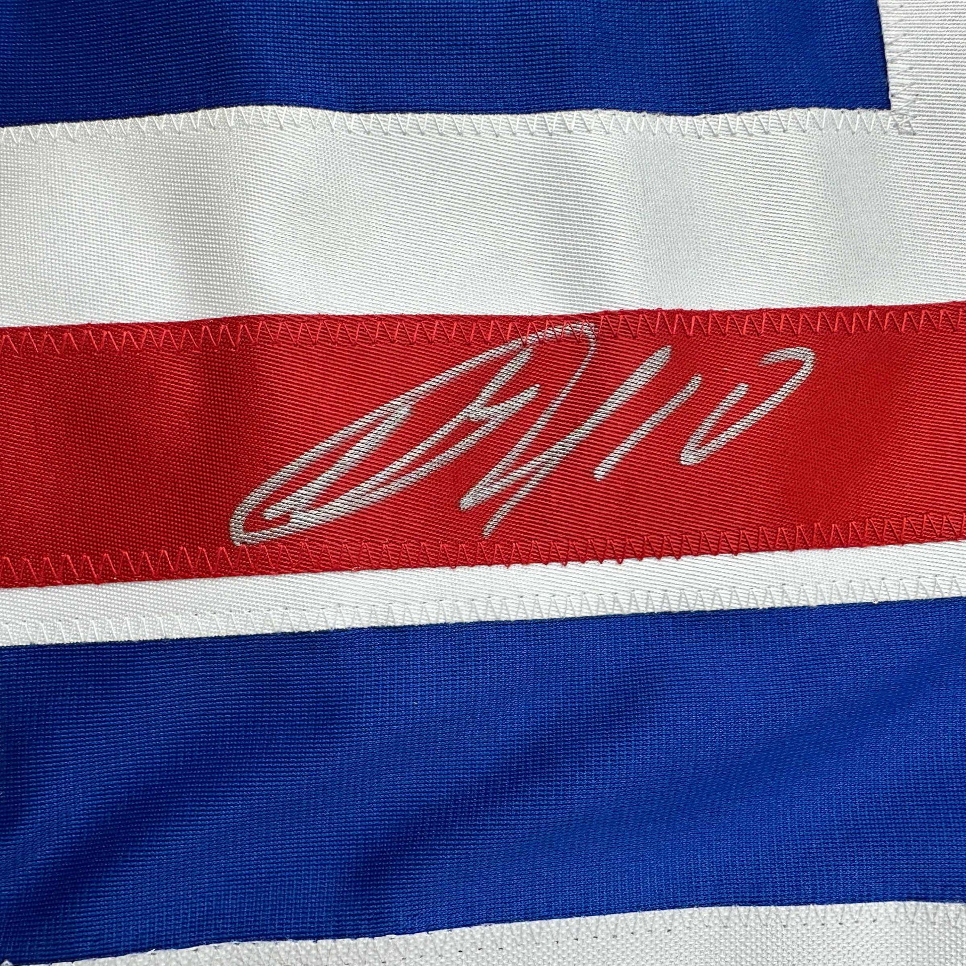 Close-up of signed red stripe on blue and white horizontally striped hockey jersey with gray cursive autograph.