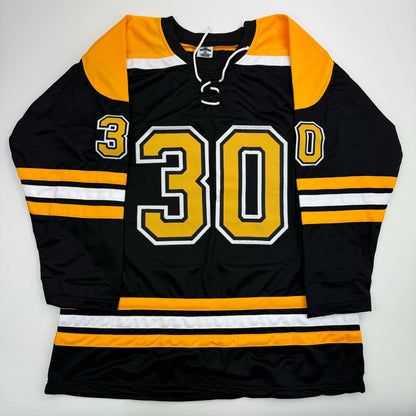 Black Boston Bruins hockey jersey with gold number 30, gold and white shoulder yoke, displayed flat against white background.