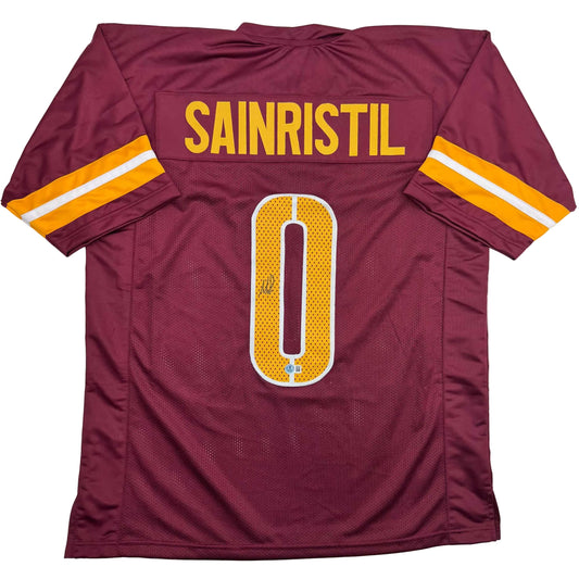 Flat lay of burgundy football jersey displaying "SAINRISTIL" nameplate and gold number 0 on back with gold and white sleeve stripes.