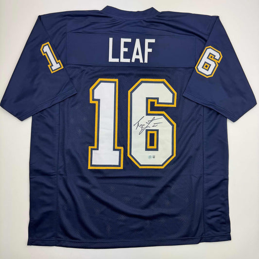 Back view of navy blue football jersey number 16 with "LEAF" nameplate, white and gold numbering, and visible autograph on right side of chest.