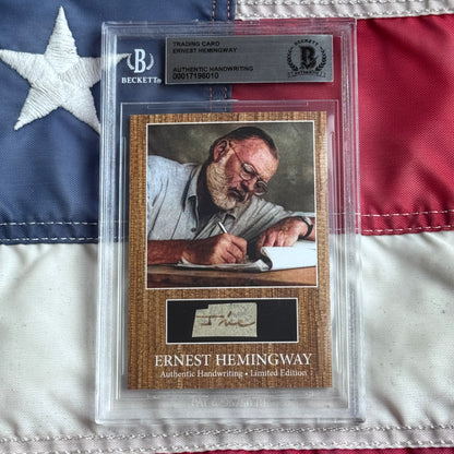 Beckett-authenticated Ernest Hemingway trading card with handwriting sample displayed in plastic case against American flag background.