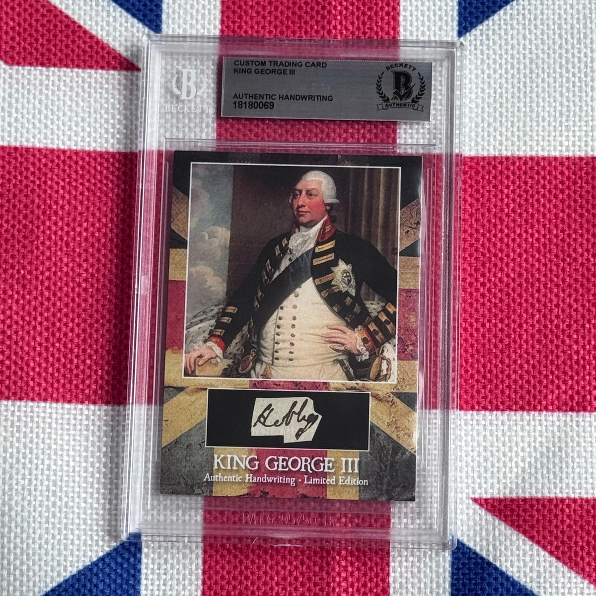 Authenticated trading card of King George III in formal military dress with white powdered hair, displayed in clear protective case against Union Jack background.