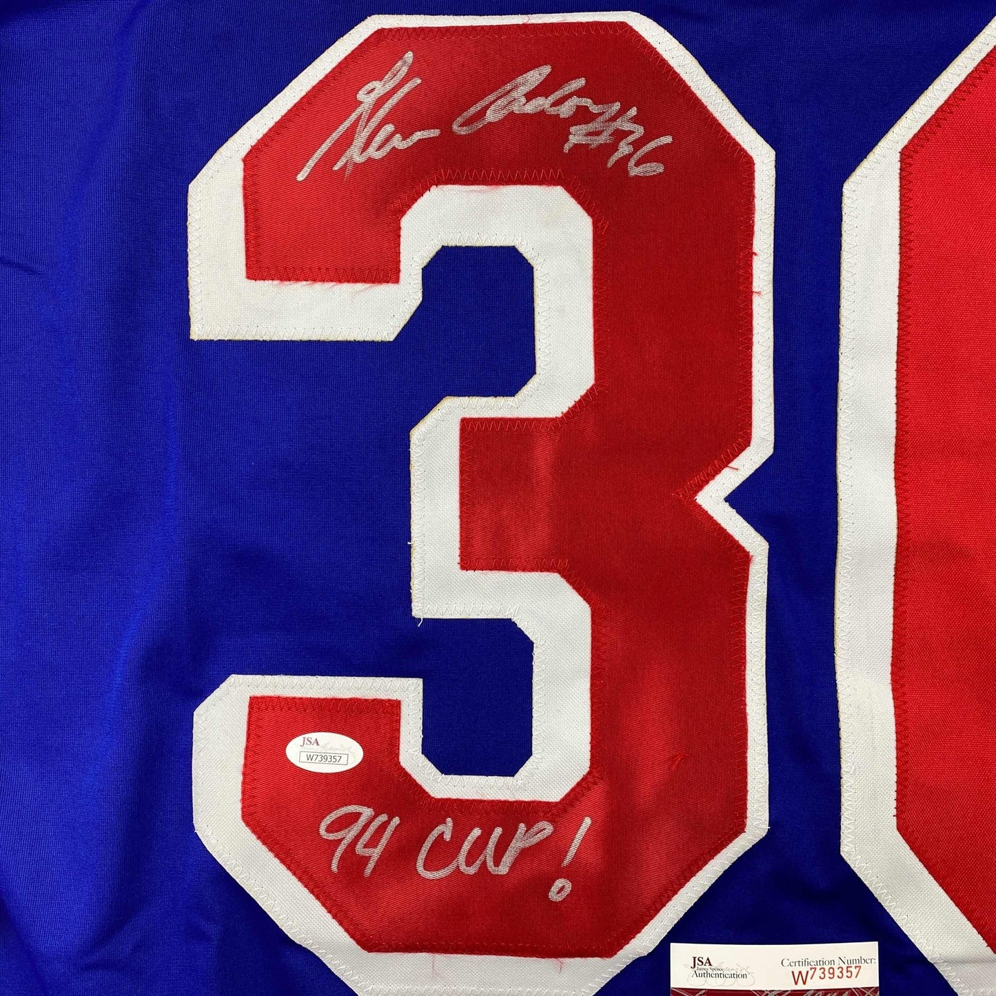 Close-up of signed blue hockey jersey number 3 with red and white stitching, showing autographed inscriptions and JSA authentication label.