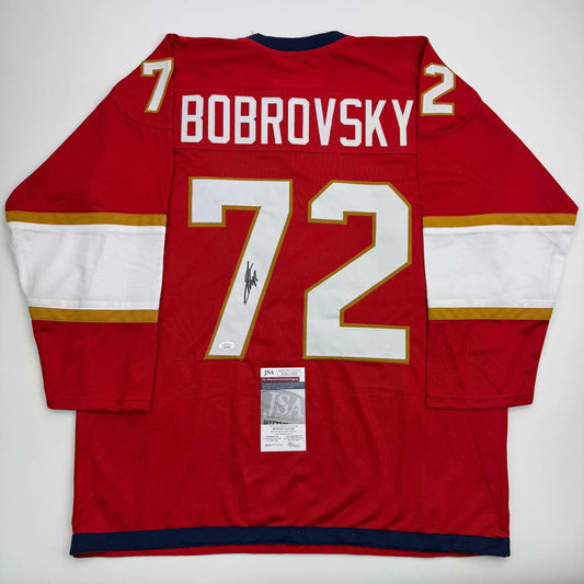 Red hockey jersey with white and gold trim, "BOBROVSKY" and number 72 printed on back, JSA authentication certificate attached below neckline.