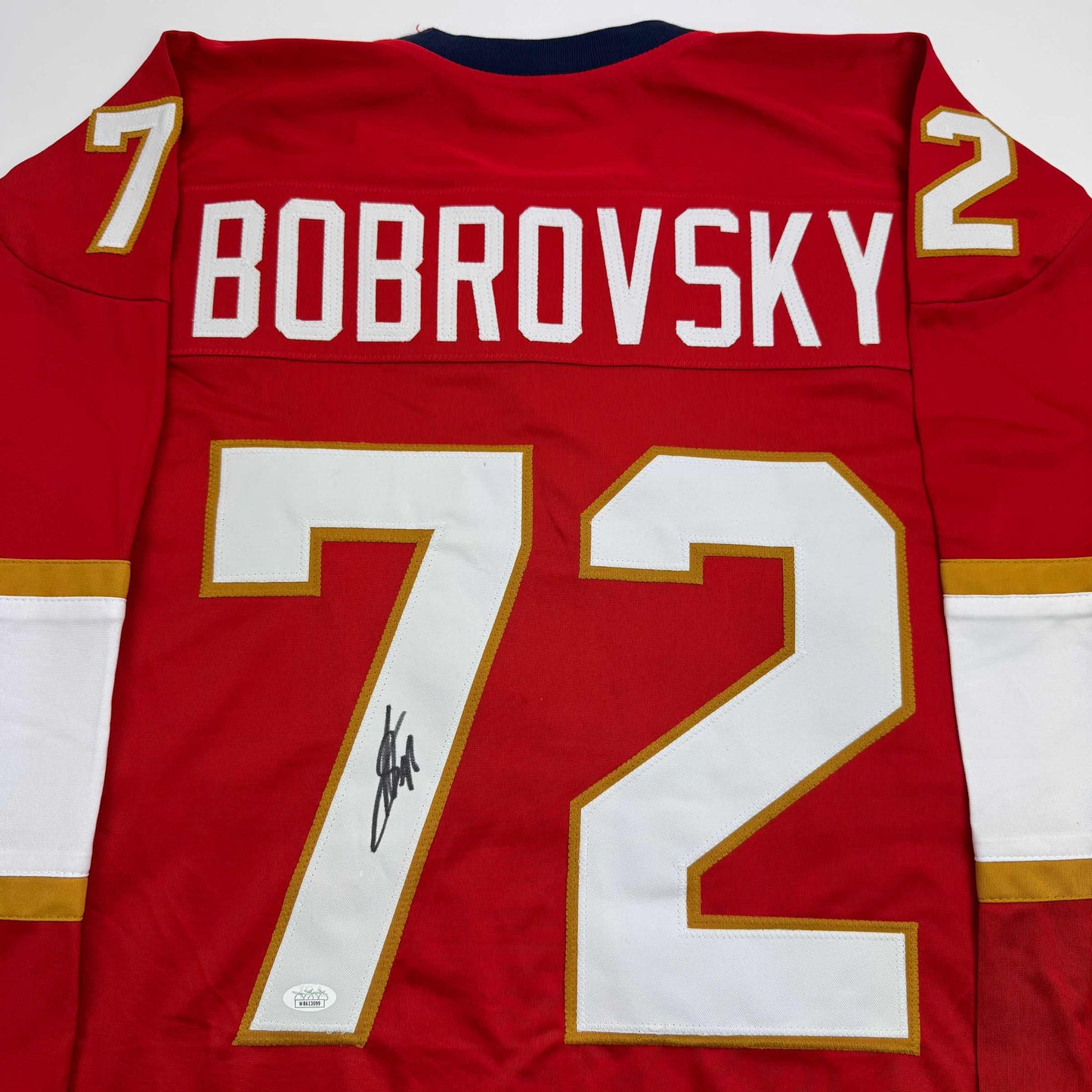 Back view of red hockey jersey with white "BOBROVSKY" nameplate, large white numbers 72 with gold trim, and autographed signature on front.