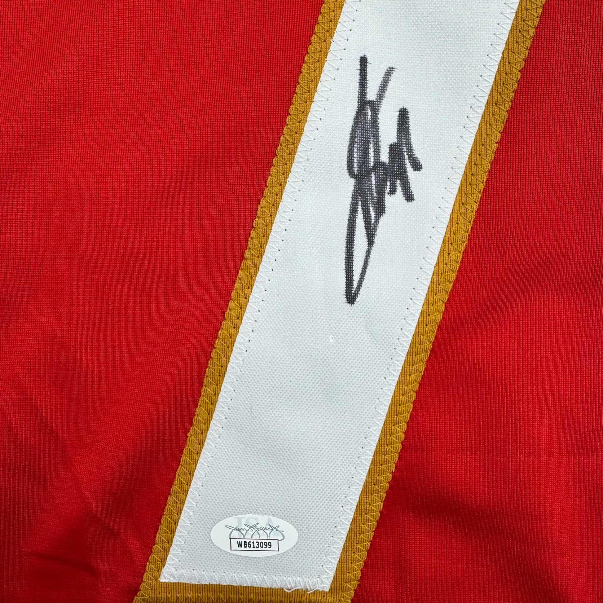 Close-up of red hockey jersey nameplate strip showing handwritten signature and JSA authentication sticker with certification number.