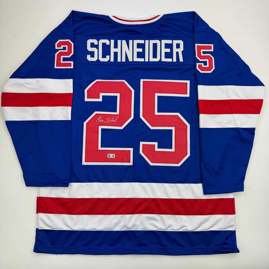 Blue, red, and white striped hockey jersey displayed flat showing back with "SCHNEIDER 25" and autograph signature visible.