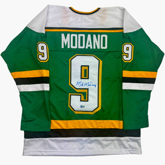 Green and white Minnesota hockey jersey number 9 with "MODANO" nameplate and blue autograph on chest, displayed flat against white background.